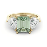 A gold ring with a large, green gemstone in the center, flanked by two smaller diamonds on either side.