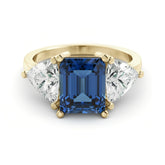 A gold ring with a large blue gemstone in the center, flanked by two smaller diamonds on either side.