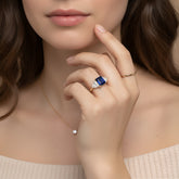 A close-up of a woman's hand wearing a ring and necklace, with her hand resting on her chin.