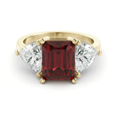 A gold ring with a large red gemstone in the center, flanked by two smaller diamonds on either side.
