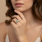 A close-up of a woman's hand wearing a ring and necklace, with her chin resting on her hand.