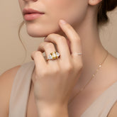 A close-up of a woman's hand wearing a gold ring with a large yellow gemstone, resting on her finger.