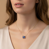 A close-up of a woman's neck and chest area wearing a gold necklace with a blue gemstone pendant.