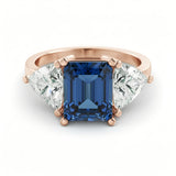 A gold ring with a large blue gemstone in the center, flanked by two smaller diamonds on either side.
