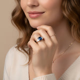 A close-up of a woman's hand wearing a ring with a blue gemstone, resting on her finger.
