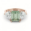 A rose gold ring with a large, green gemstone in the center, flanked by two smaller diamonds on either side.