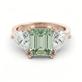 A rose gold ring with a large, green gemstone in the center, flanked by two smaller diamonds on either side.