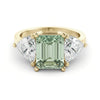 A gold ring with a large, green gemstone in the center, flanked by two smaller diamonds on either side.
