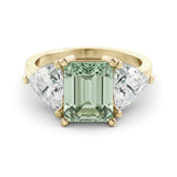 A gold ring with a large, green gemstone in the center, flanked by two smaller diamonds on either side.