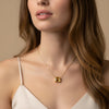 A close-up of a woman's neck and chest area, featuring a gold necklace with a large gemstone pendant.