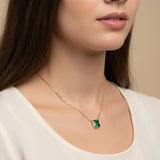 A close-up of a woman's neck and chest area wearing a gold necklace with a green gemstone pendant.