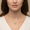 A close-up of a woman's neck and chest area, with a gold necklace featuring a large green gemstone pendant.