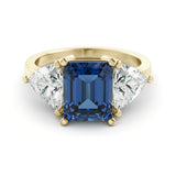A gold ring with a large blue gemstone in the center, flanked by two smaller diamonds on either side.