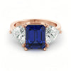 A rose gold ring with a large blue gemstone in the center, flanked by two smaller diamonds on either side.