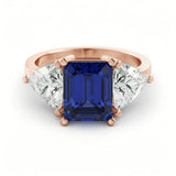 A rose gold ring with a large blue gemstone in the center, flanked by two smaller diamonds on either side.