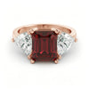 A rose gold ring with a large, deep red gemstone in the center, flanked by two smaller diamonds on either side.