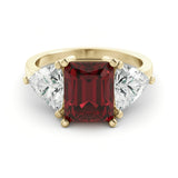 A gold ring with a large red gemstone in the center, flanked by two smaller diamonds on either side.