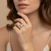 A close-up of a woman's hand wearing a ring and necklace, with her chin resting on her hand.
