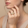 A close-up of a woman's hand wearing a gold ring with a large yellow gemstone, resting on her finger.