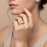 A close-up of a woman's hand wearing a gold ring with a large yellow gemstone, resting on her finger.