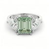 A silver ring with a large, green gemstone in the center, surrounded by smaller diamonds on either side.